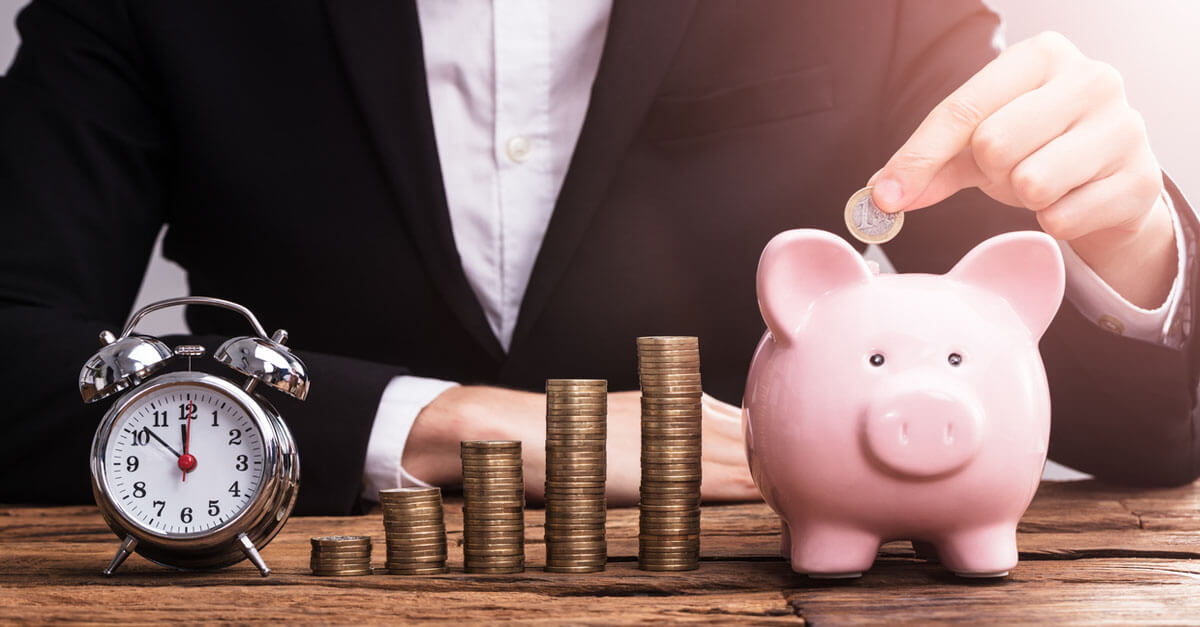 Ein Wecker, gestapelte Münzen und ein Sparschwein stehen nebeneinander.