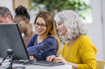 Erziehungswissenschaftlerin in der Erwachsenenbildung erklärt einer Kursteilnehmerin etwas am PC