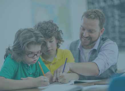 Heilpädagoge erklärt Kindern etwas am Schreibtisch