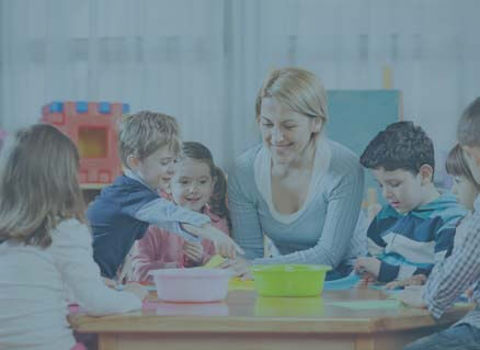 Kinder sitzen mit einer Pädagogin am Tisch